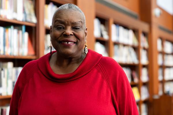 Vivian Fisher, in a red sweater, smiles for a portrait in the Enoch Pratt Central Library’s Juanita C. Burns Memorial African American Reading Room.
