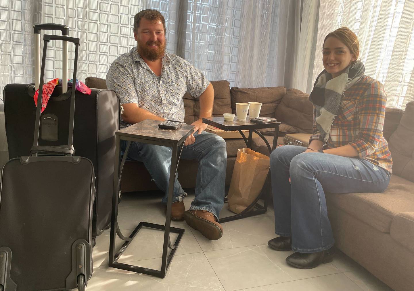 A man and a woman sit on the couch of an airport hotel with their luggage.