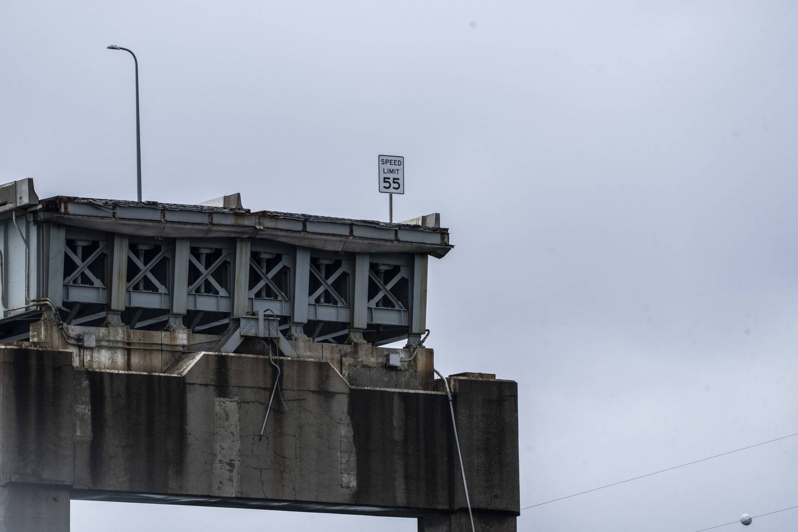 A speed limit sign instructing drivers to not exceed 55mph sits at the end of what is left of the Key Bridge.
