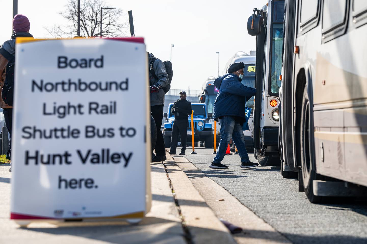 A rider boards a shuttle bus. A sign reading "Board Northbound Light Rail Shuttle Bus to Hunt Valley here" is in the left foreground.