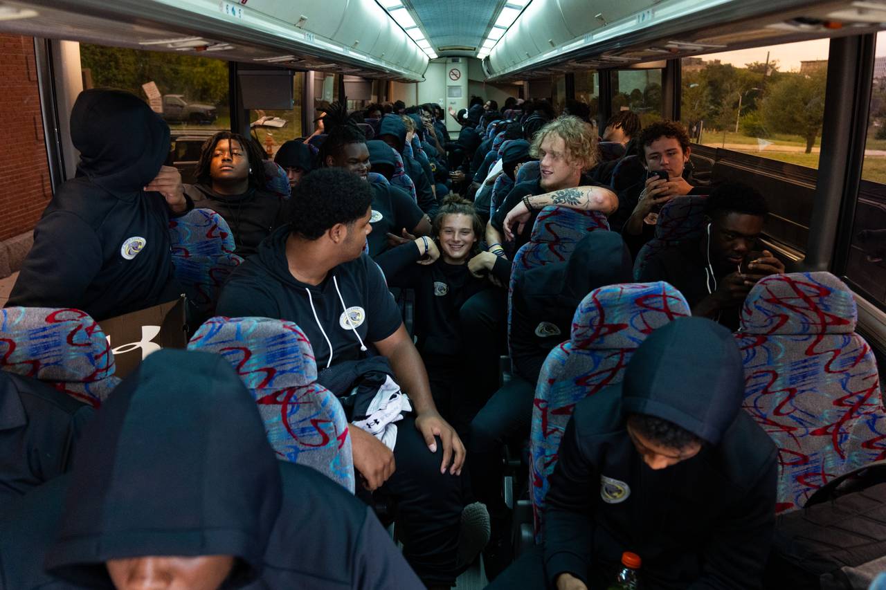 Players pack the coach bus, one sitting in the center aisle and smiling.
