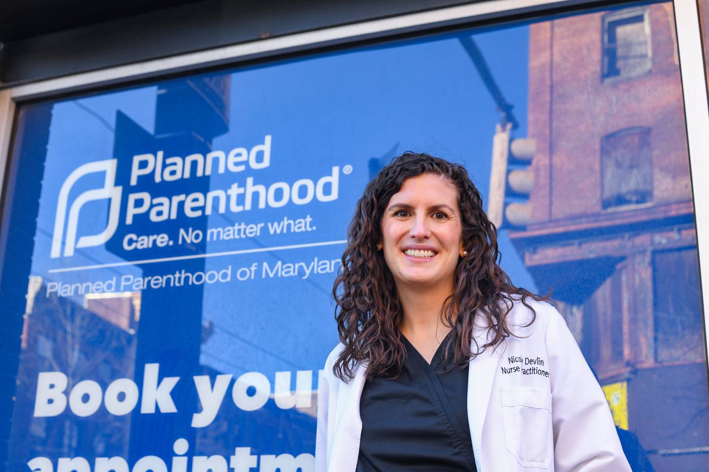 A nurse in a white medical coat, stands in front of a planned Parenthood sign to take a portrait..