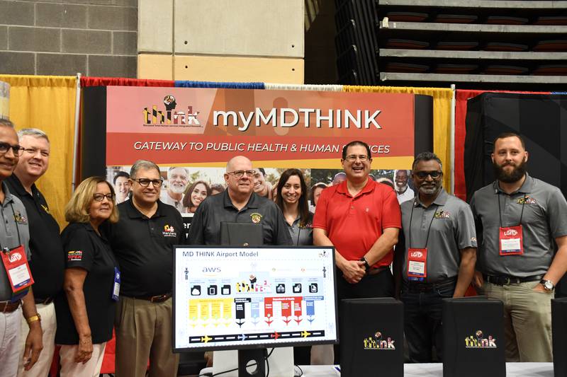 Maryland Gov. Larry Hogan, center, and top aide Christopher Shank, in red shirt, pose for pictures at the MD THINK booth at the Maryland Association of Counties Conference in Ocean City on Friday, Aug. 19, 2022.
