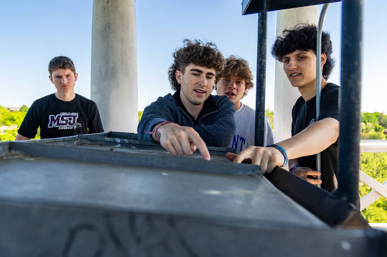 Christopher Larkin, center, shows his friends where his family has signed their names atop Mount Saint Joseph’s historic tower on May 1, 2024.