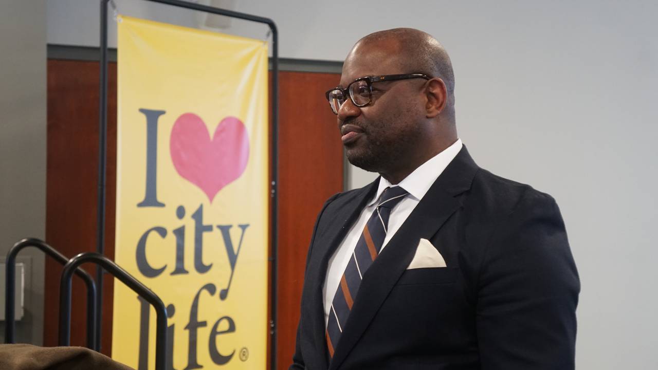 A profile image of a man dressed in a suit and tie standing in front of a yellow banner that says "I love city life."