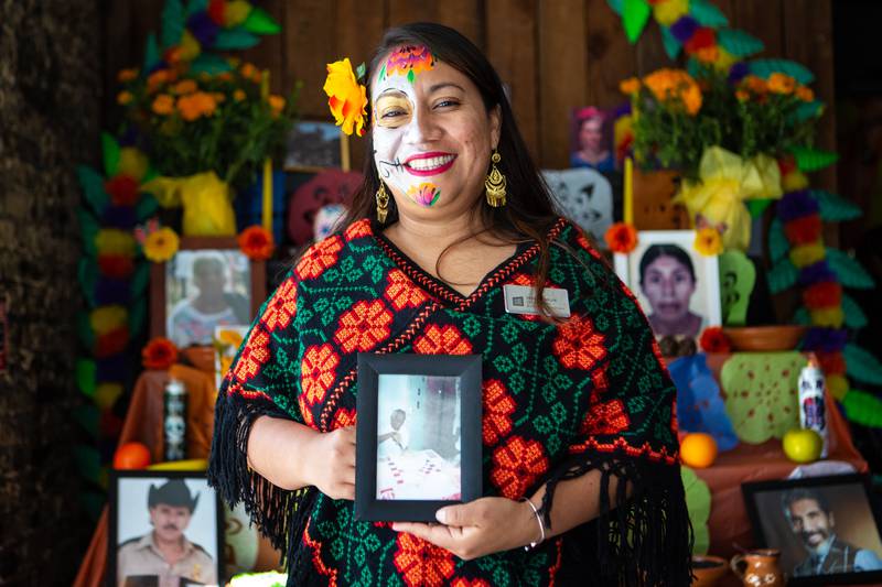 11/5/22 – Yesenia Mejia Herrera shows a picture of her grandfather in front of the Artesanas' altar at the Creative Alliance's Día de los Muertos celebration on Saturday.