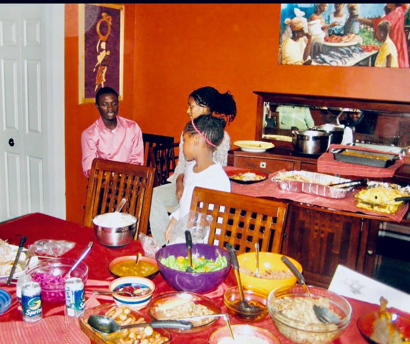 A child, man and woman stand behind a dining room table with a variety of Thanksgiving foods.