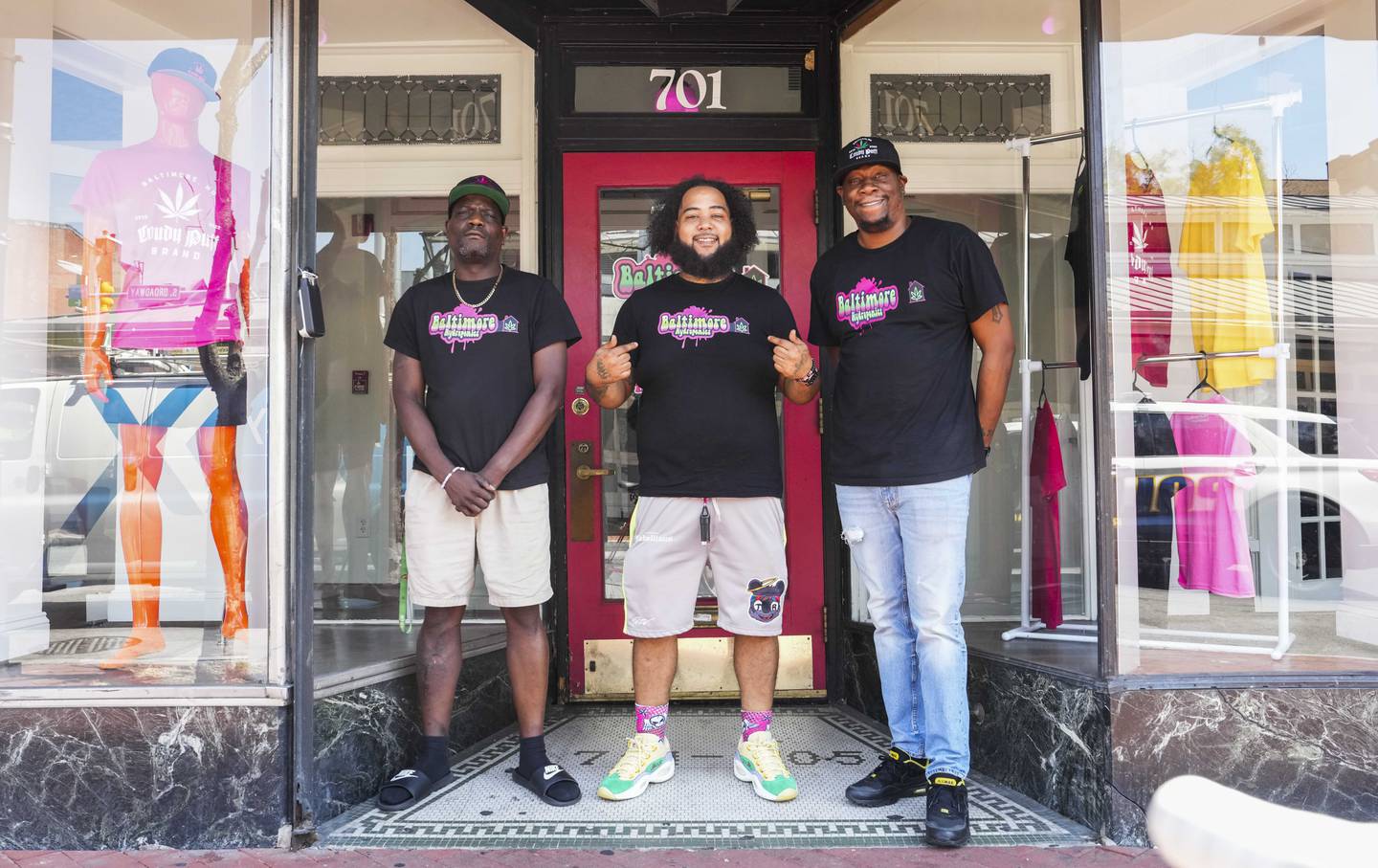 Three men wearing black t-shirts stand in front of the door to their Fells Point shop.