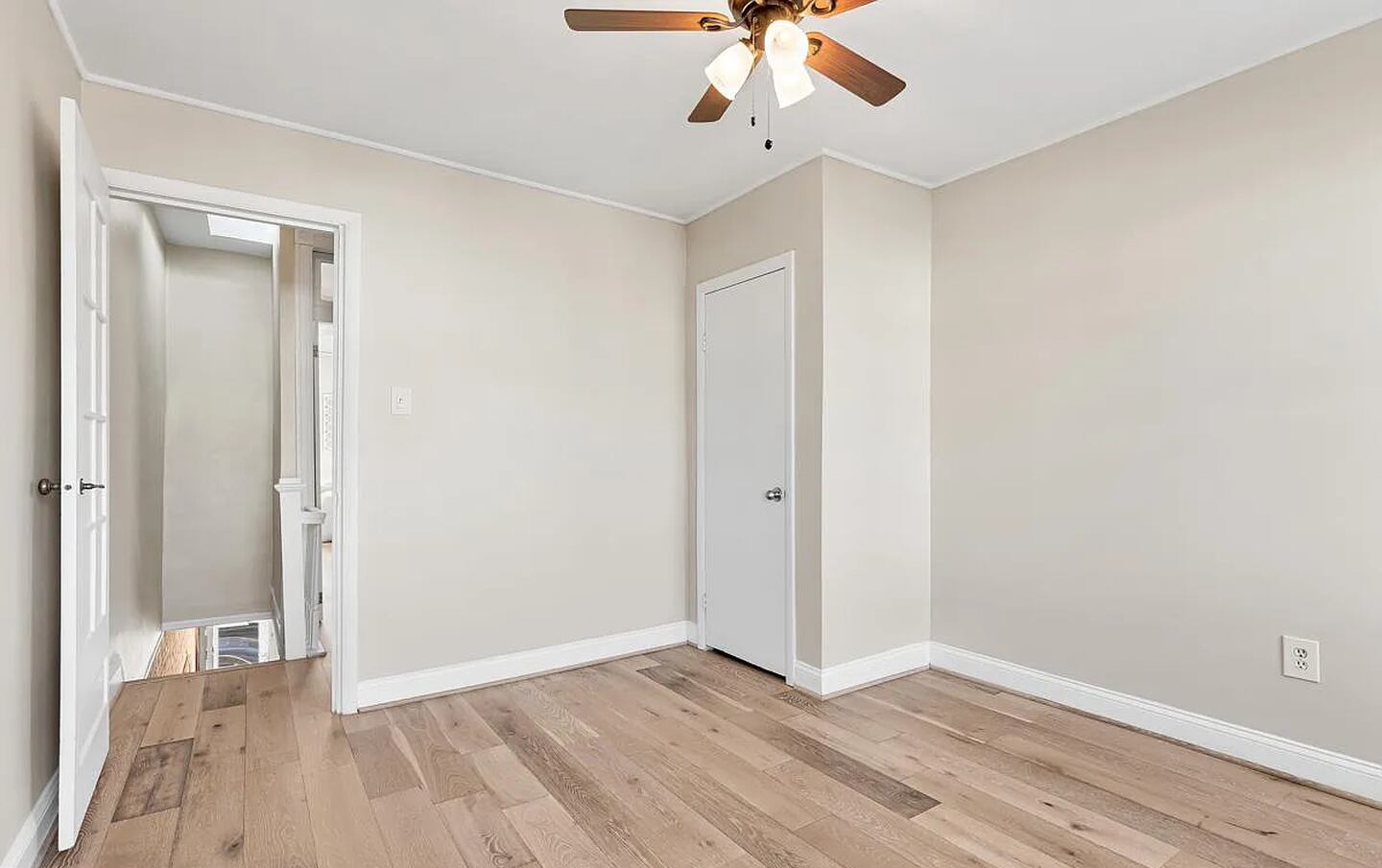 An upstairs bedroom with no furniture. There's hardwood floors with a light stain, beige walls and white trim.