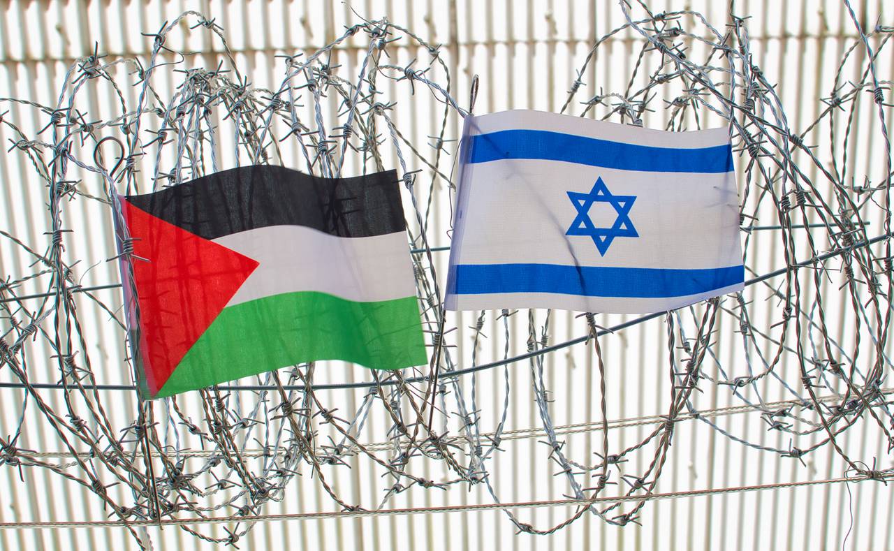 Image shows flags for Israel, Palestine on barbed wire.