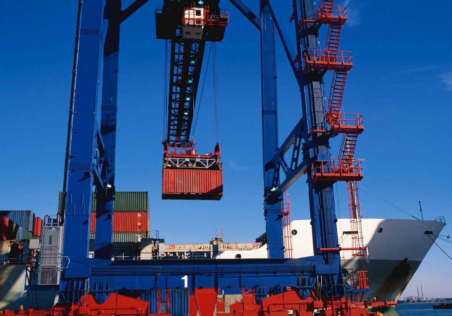 A blue crane loads a red container onto a cargo ship at the Port of Baltimore.
