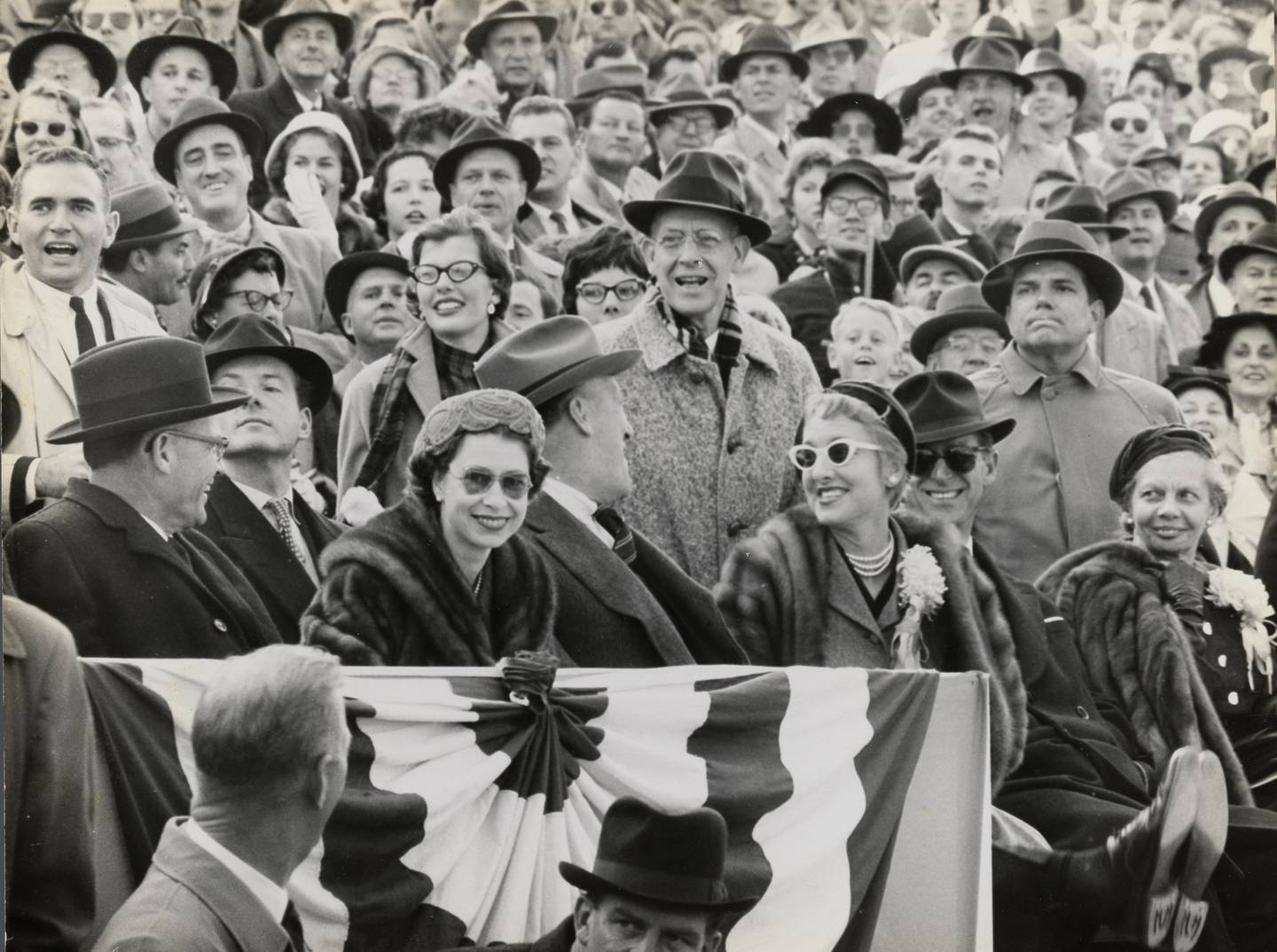 Queen Elizabeth II smiles as she sits in the stands at a football game between the University of Maryland and the University of North Carolina, October 19, 1957. In her row, from left to right: University of Maryland President Wilson Elkins, the Queen, Governor Theodore McKeldin, Mrs. Dorothy Elkins, and Prince Philip, Duke of Edinburgh. Courtesy of University of Maryland Archives.