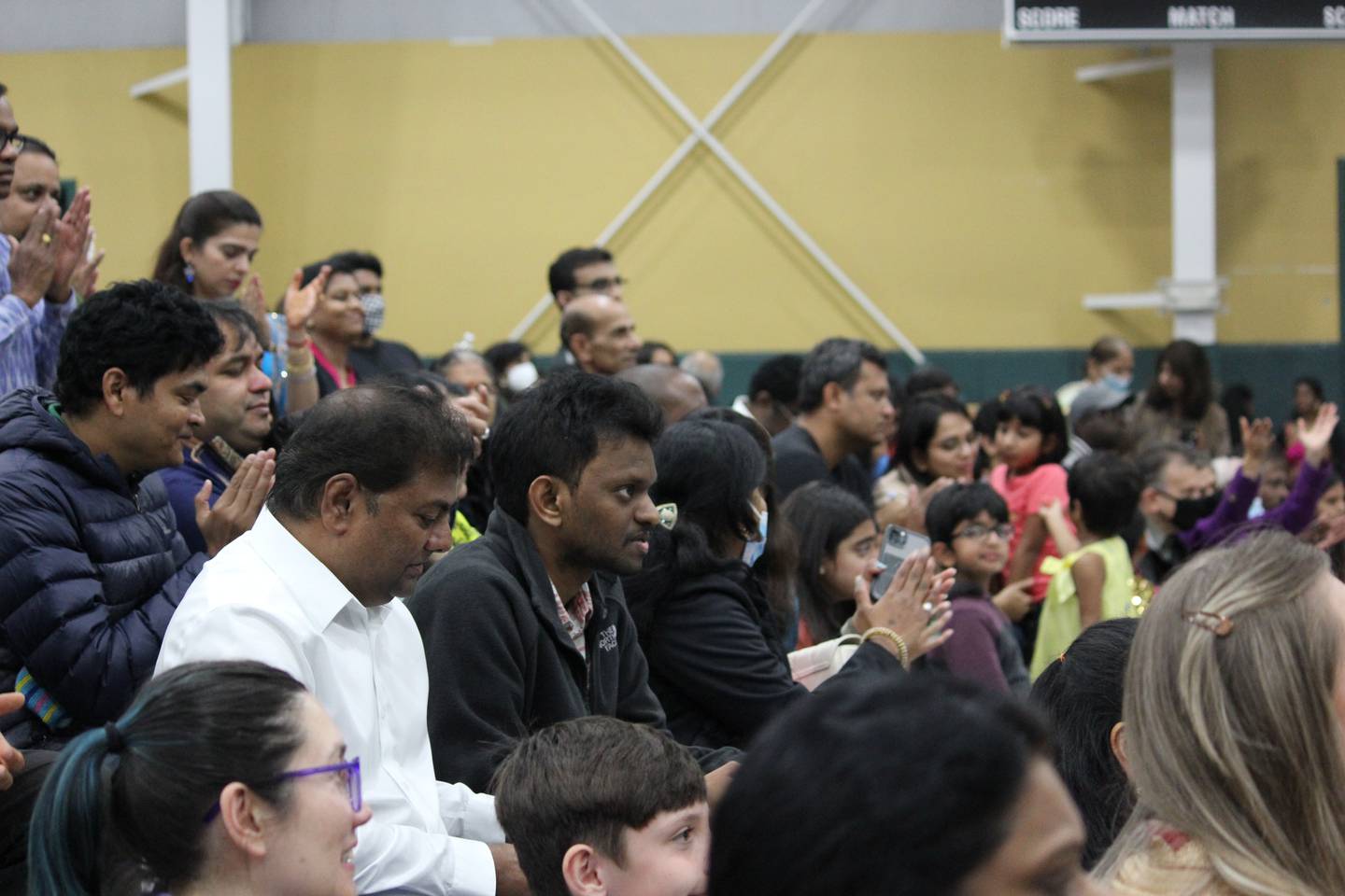 A crowd of Indian American residents sit in a large venue. Some are clapping.