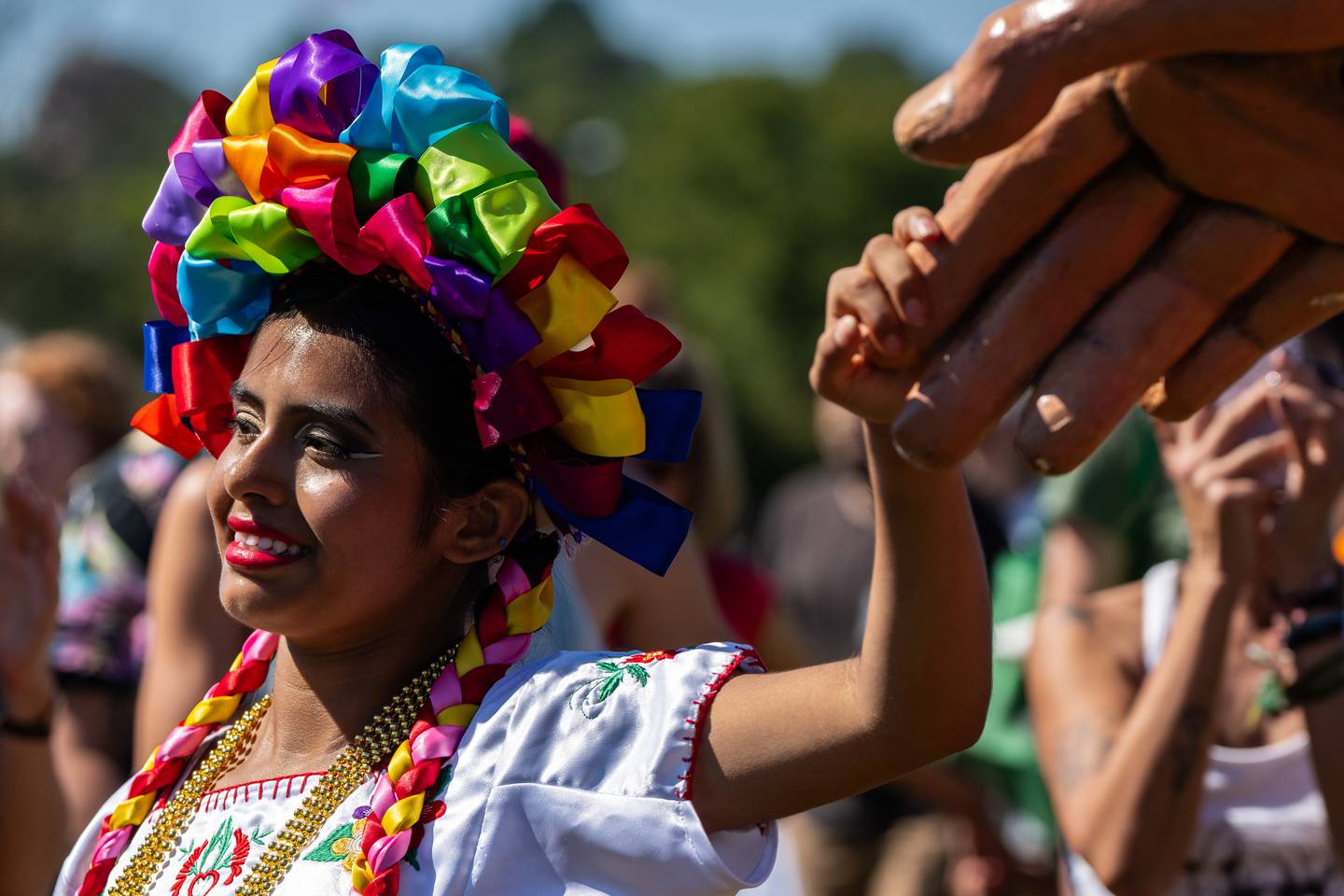 Lele, a Mexican dancer in a rainbow headdress and a marigold necklace, holds Amal's hand.