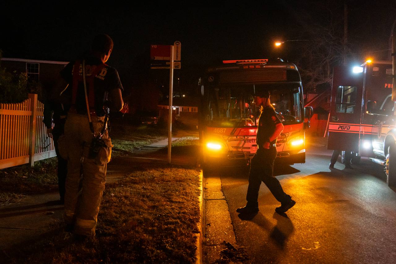 Firefighters Greyson Sheppard, left, and Nick Bowen, right, walk over to speak with a police officer about an abandoned Metro bus. Bowen is rim lit by the lights of the Metro bus.