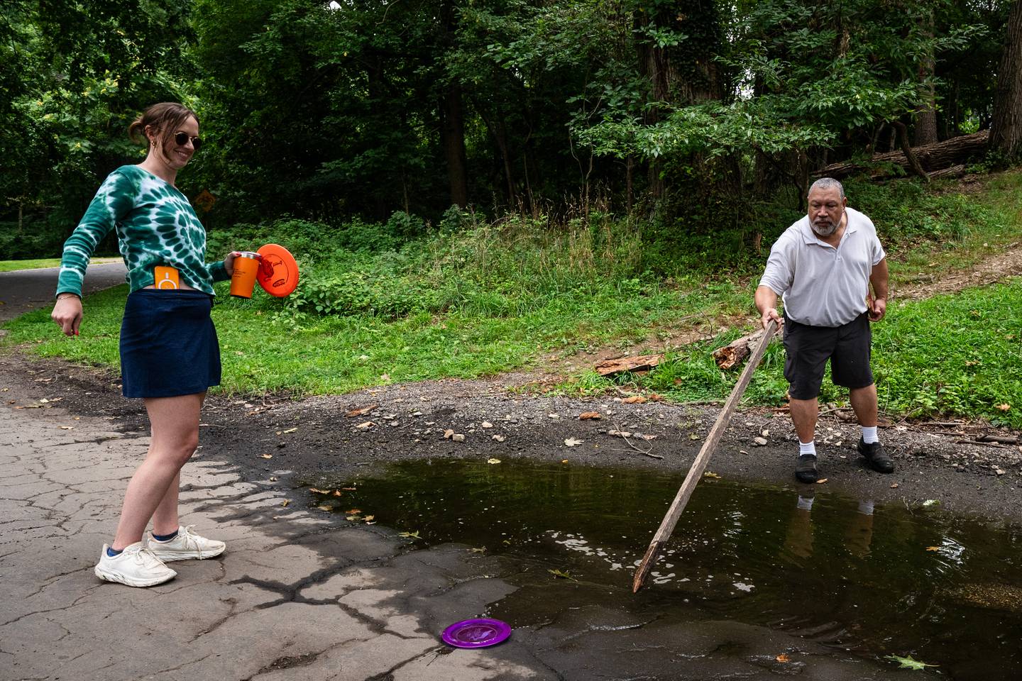 Baltimore Banner reporter Emily Sullivan laughs as Baltimore Comptroller Bill Henry fishes a disc out of a pool of water.