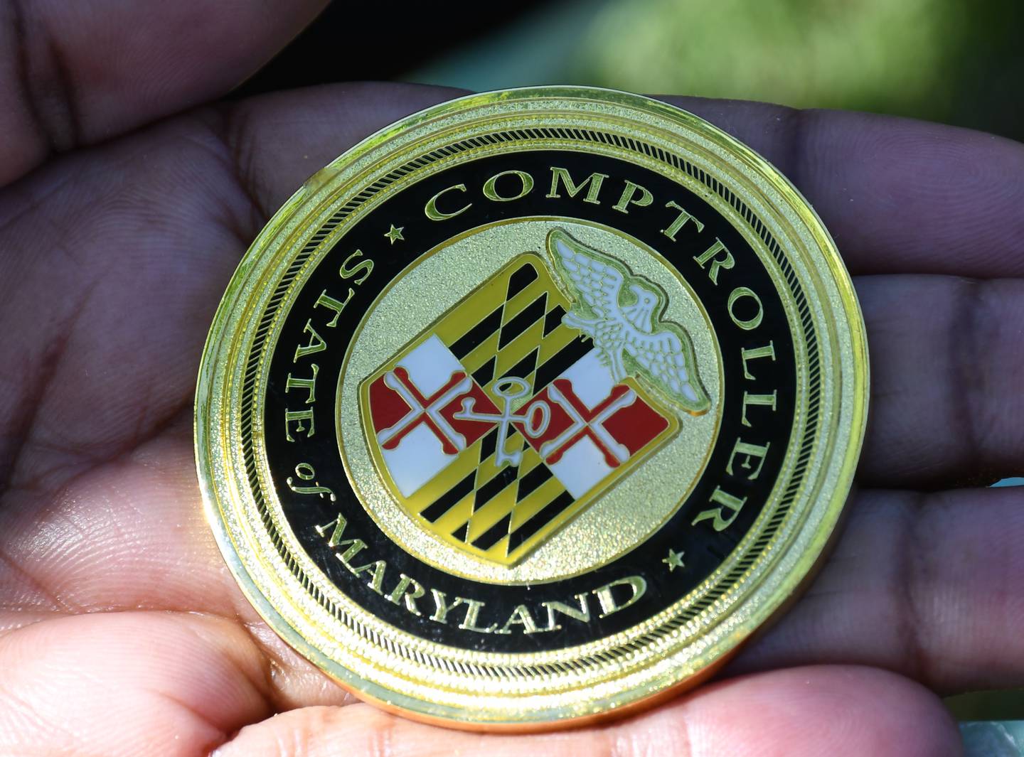 A woman holds a commemorative coin given to her by Maryland Comptroller Peter Franchot at Baltimore's AFRAM festival on June 19, 2022. Franchot, who is a Democratic candidate for governor, frequently hands out the coins, especially to people with military or law enforcement backgrounds. The other side says: "In Recognition of Excellence, Service, & Sacrifice" and carries Franchot's name and title.