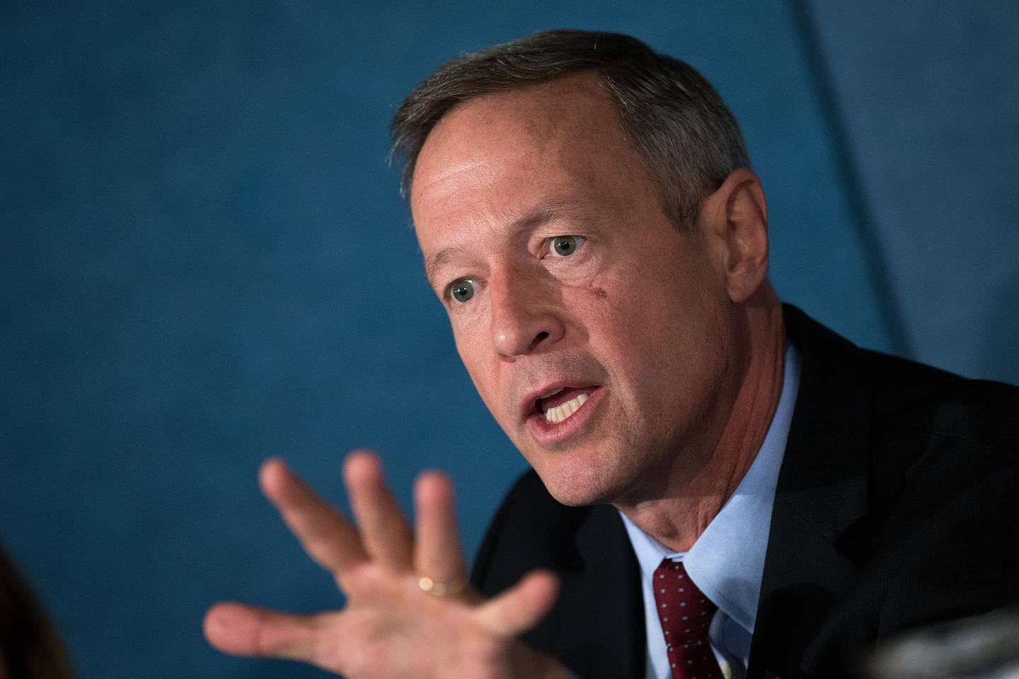 Martin O'Malley, wearing a dark suit and tie, holds his hand up in front of himself as he speaks.