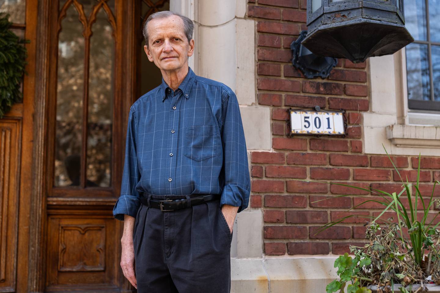 Richard Oloizia poses for a portrait, left hand in his pocket, in front of the brick front entrance of Tudor Arms Apartments.