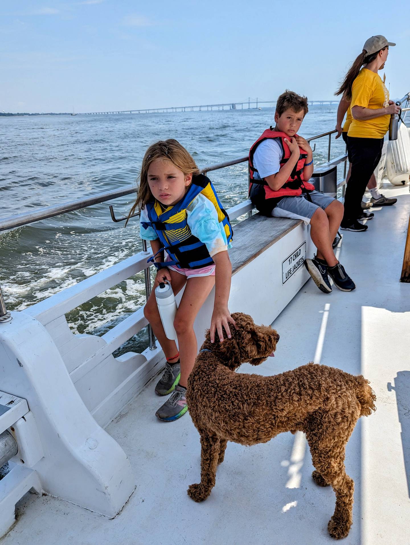 Pearl, one of the summer campers aboard the Wilma Lee, reaches out to Ollie, a moyen poodle who serves as the official boat dog for the historic skipjack.
