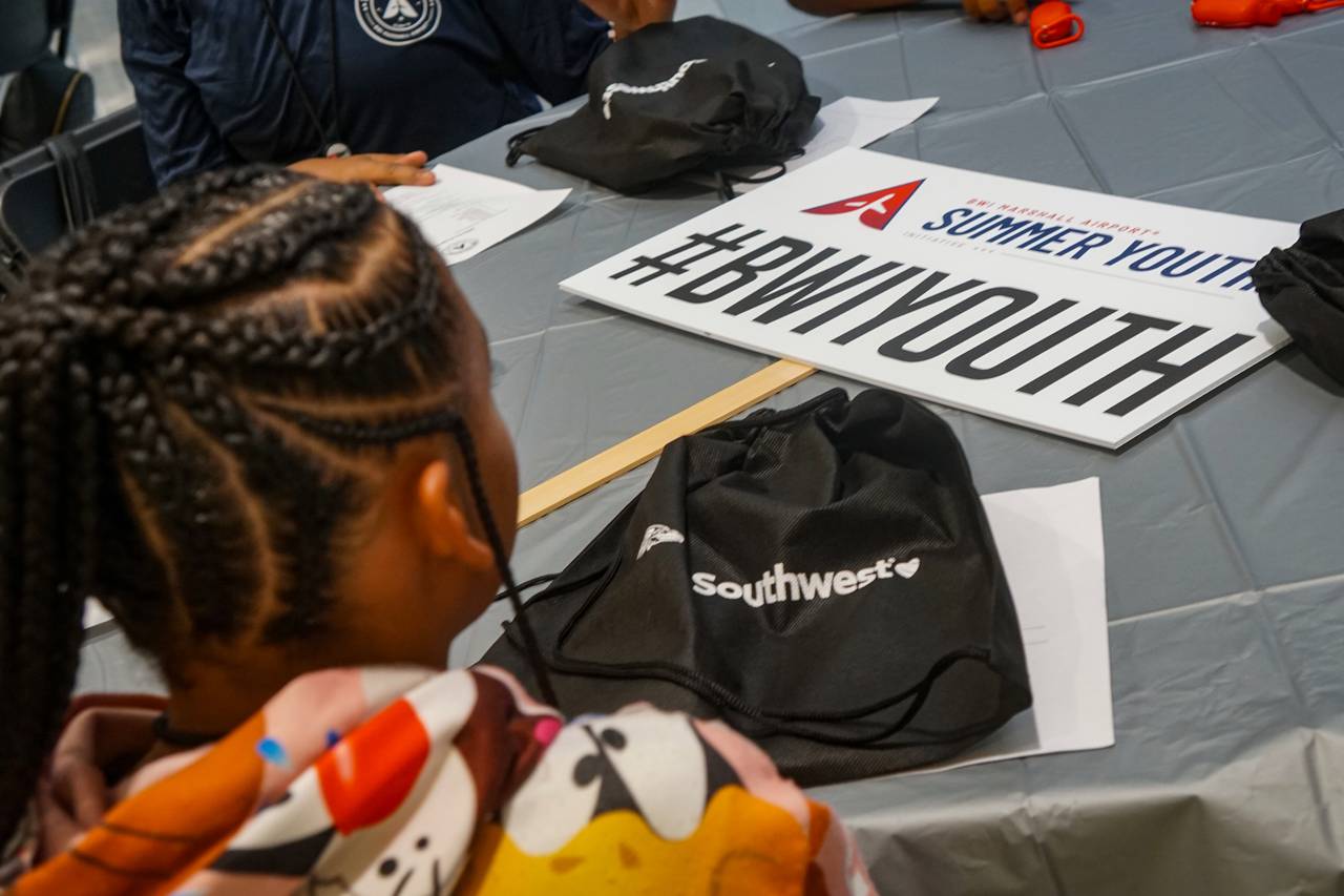A sign for BWI's Summer Youth Initiative lies on a table, as seen from behind the shoulder of a young camper.