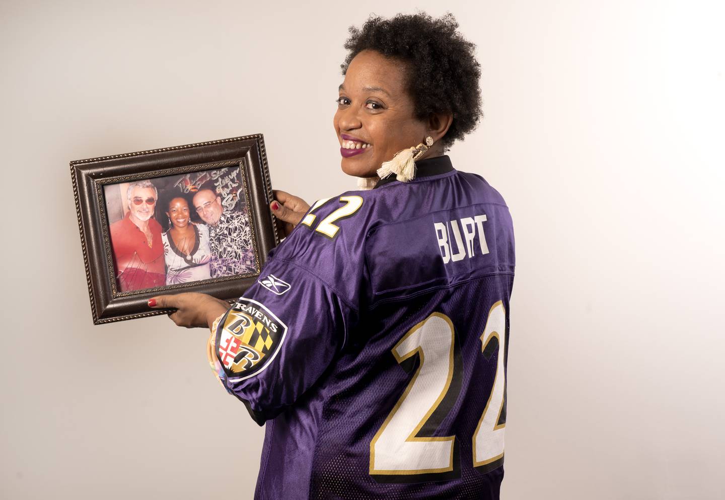 Leslie Streeter wears a jersey given to her by actor Burt Reynolds and holds a photo or (l to r) Burt Reynolds, Leslie Gray Streeter and her husband  Scott Zervitz.