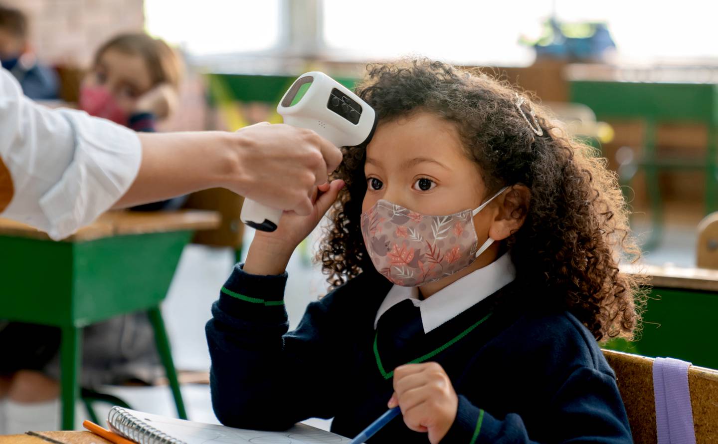 Latin American teacher checking the temperature of a girl at school using an infrared thermometer during the COVID-19 pandemic