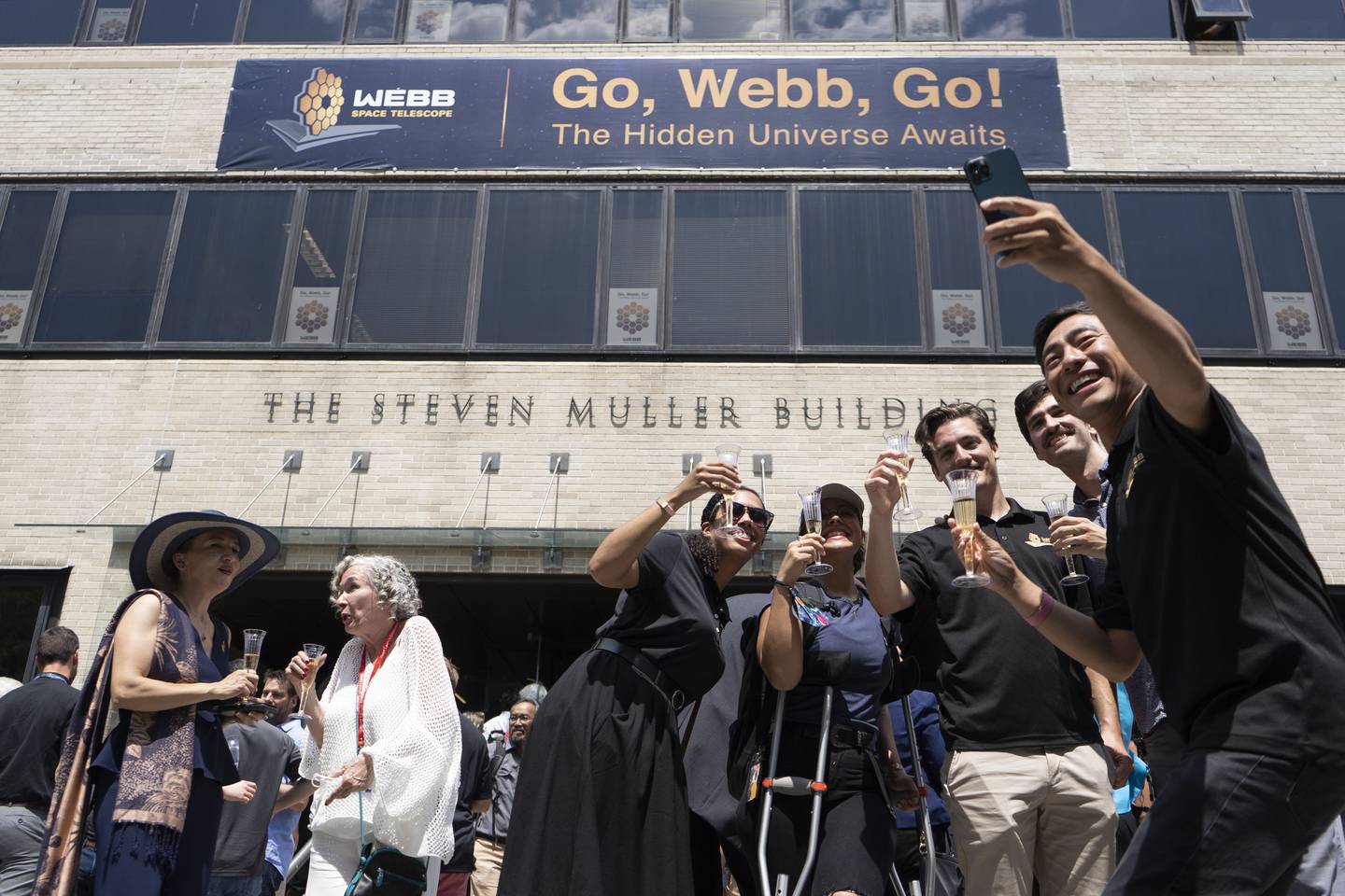 Attendees take a selfie with the banner outside of the Steven Muller Building at the James Webb Space Telescope Science Launch.