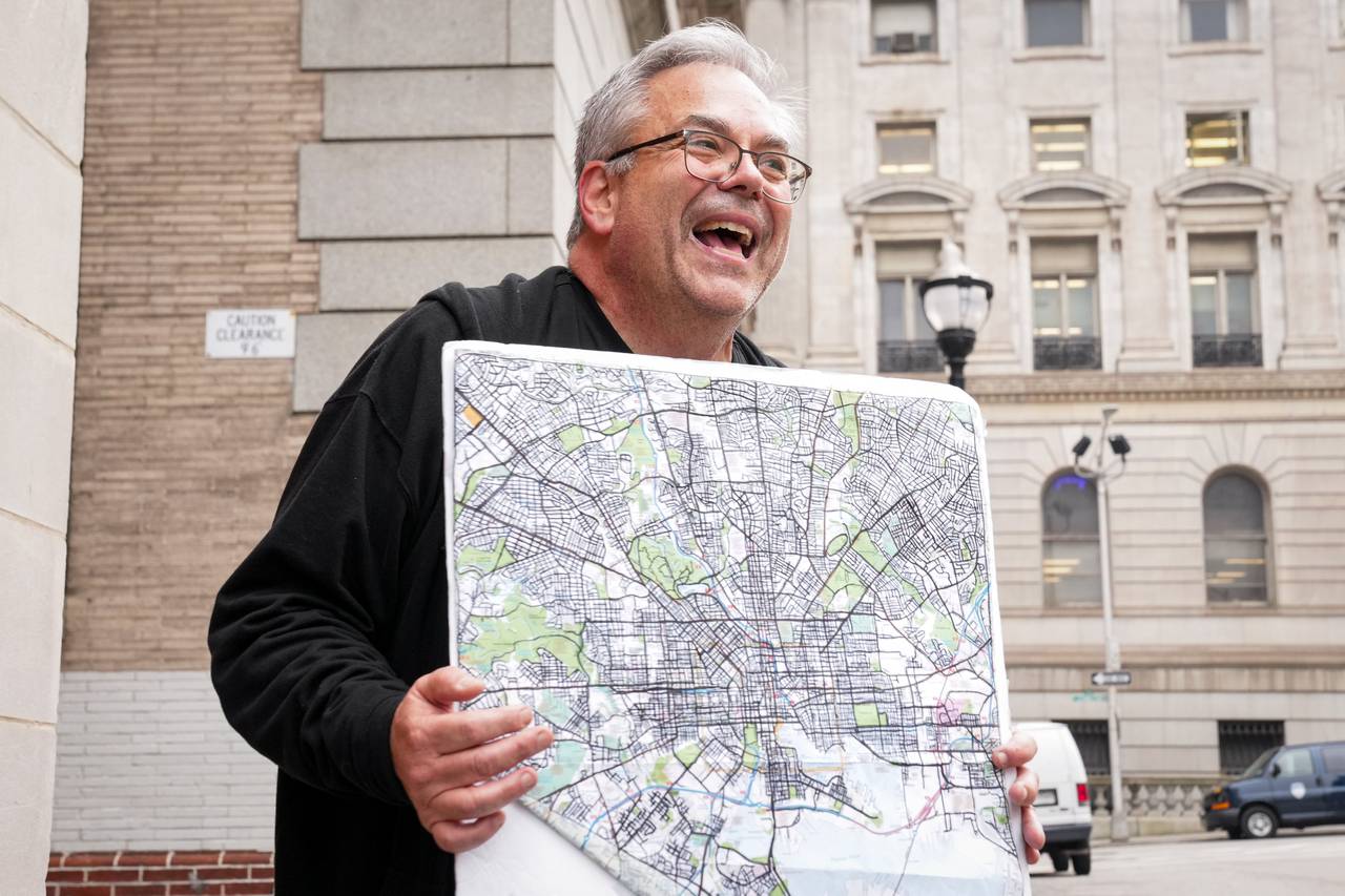 Michael Lisicky proudly holds up his completed map of Baltimore at the top of Dark Lane in downtown Baltimore on February 12, 2024. For the last eight months, Lisicky has been working to complete his goal of running on every street in Baltimore, and would mark each street in sharpie after running through it.