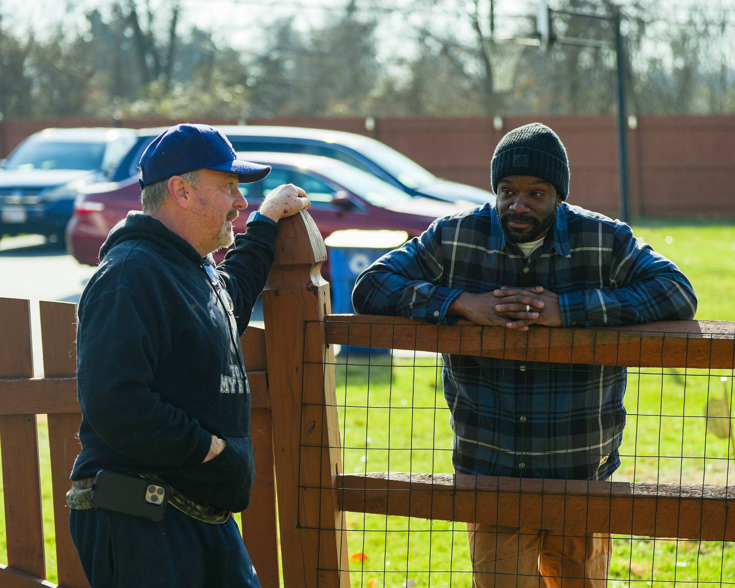 Two men talk over a wooden gate as they wait for the potential capture of an injured stray pitbull.
