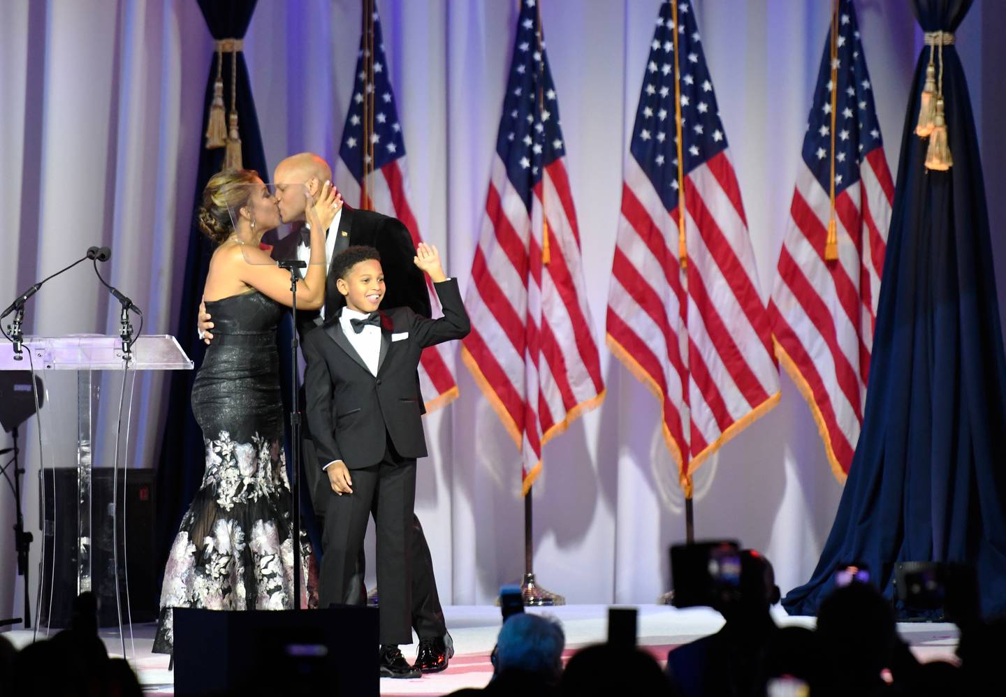 Gov. Wes Moore, second from left, kisses his wife, Dawn, as their son, James, 11, waves during Moore's inaugural ball, Wednesday, Jan. 18, 2023, in Baltimore. (Steve Ruark for the Baltimore Banner)