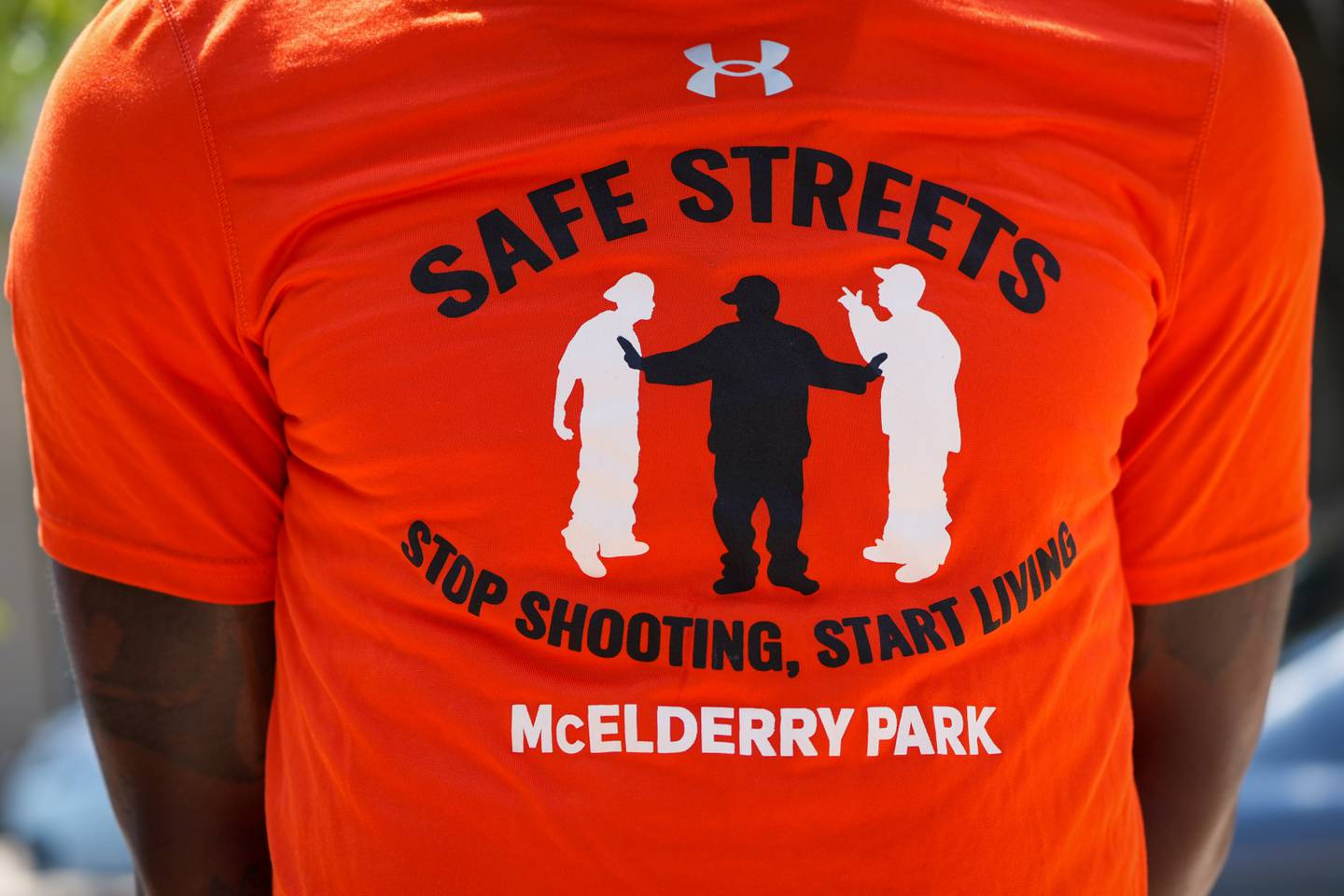 A man wearing a Safe Streets shirt stands to the side as officials speak at a press conference outside Tench Tilghman Elementary/Middle School on 8/24/22.