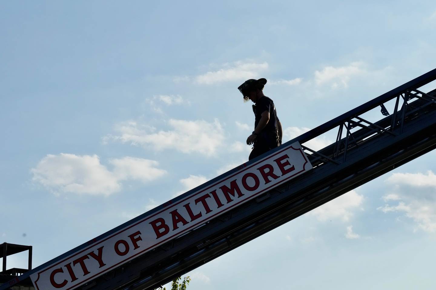 A firefighter is backlit as he walks down the ladder of a firetruck.