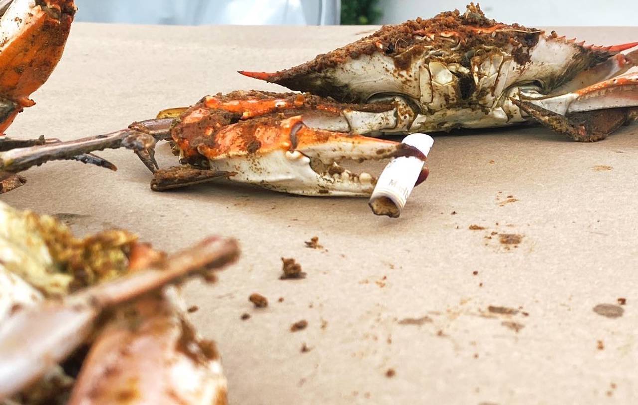 A crab seasoned with Old Bay sports a cigarette in its claw.