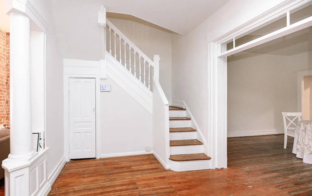 A photo of wooden stairway with white railings that opens up into a wider room with wooden floors.