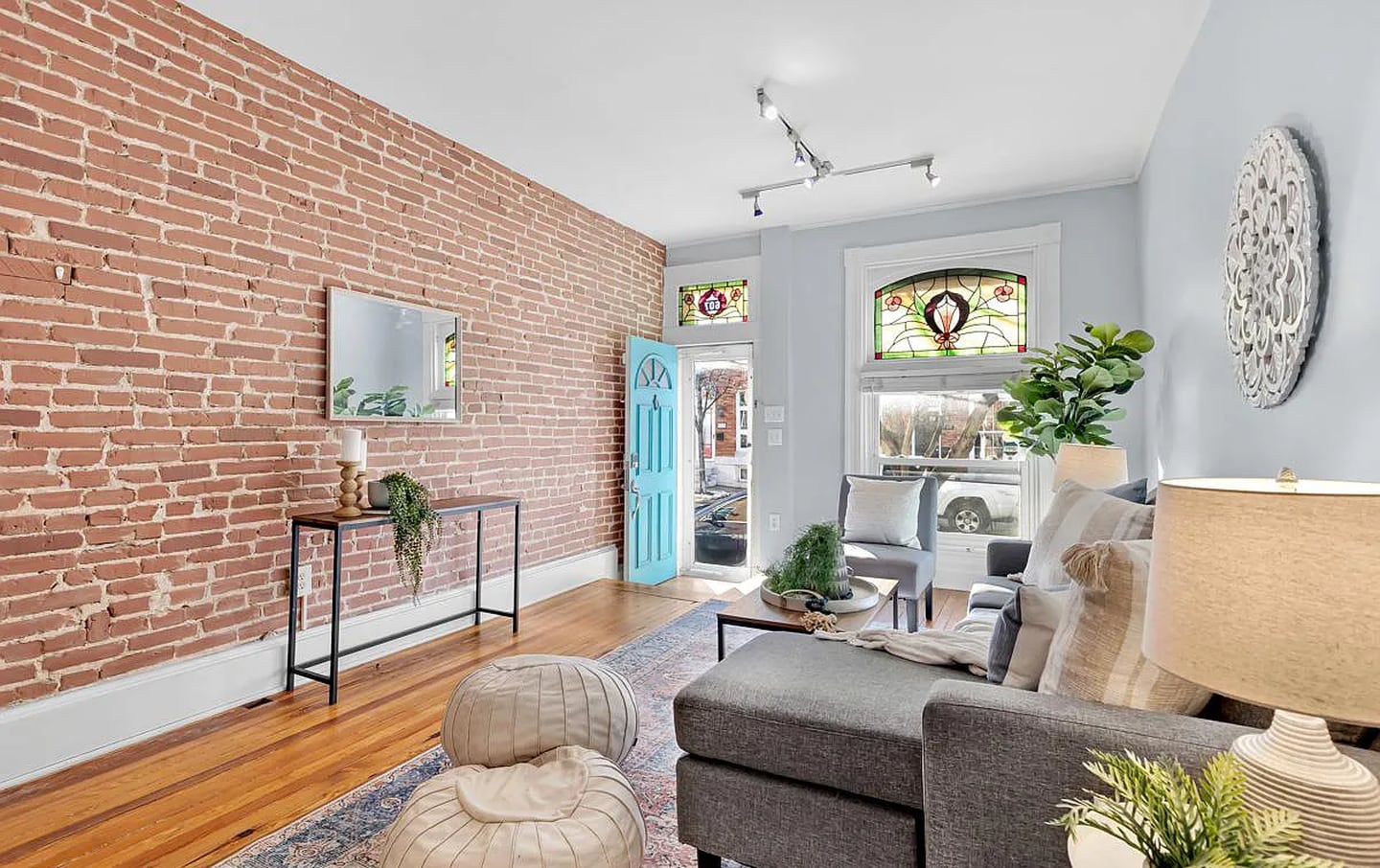 A front room with an exposed brick wall, white trim, blonde hardwood floors, a stained glass transom and window.
