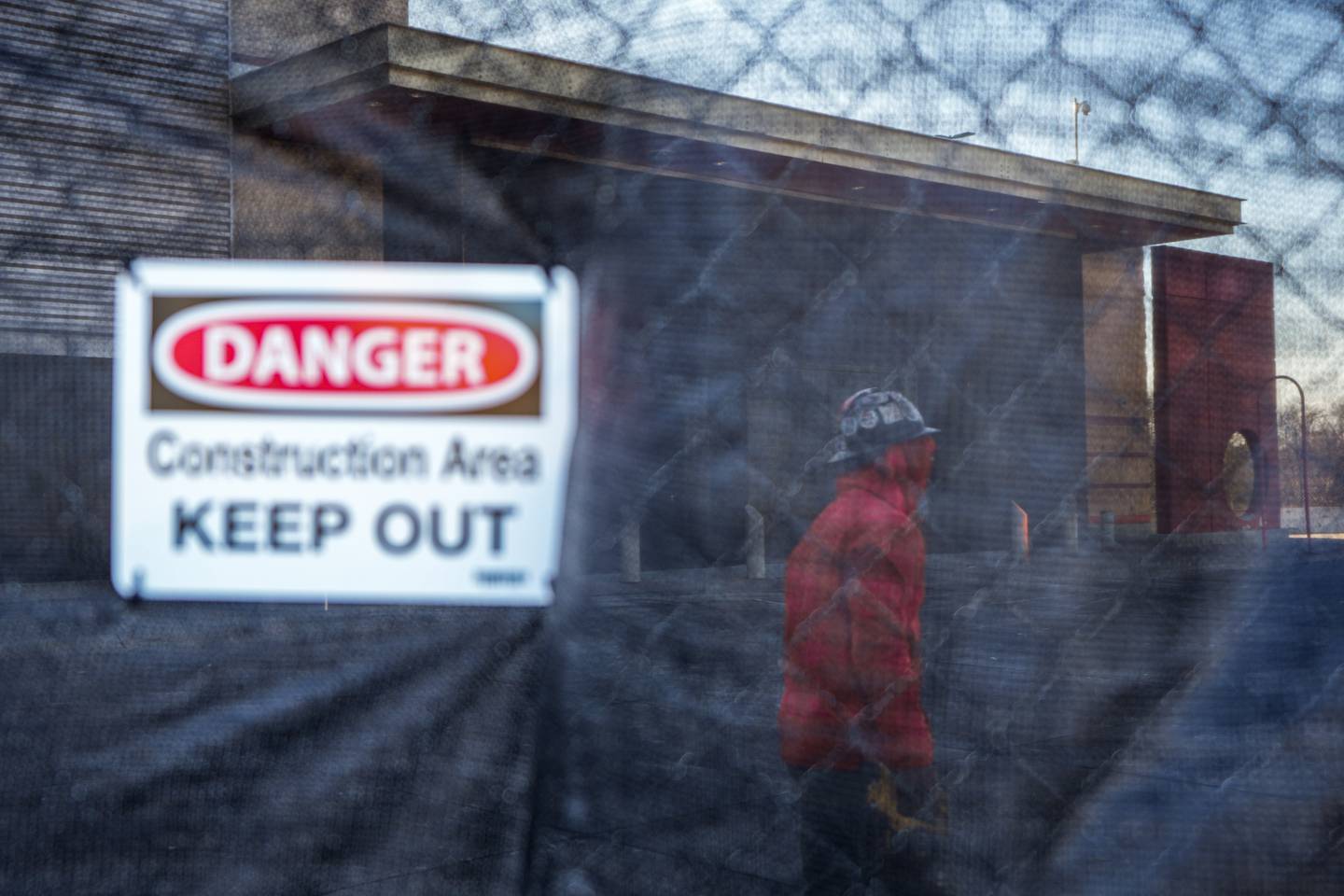 Seen through a chainlink fence covered in black fabric, a construction worker walks past the old Target building at Mondawmin Mall on 12/13/22.