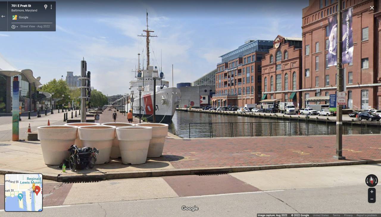 Google map screenshot of East Pratt Street showing unhoused man with wheelchair resting near flower pots before the "Baby Shark" speaker went up. Google image