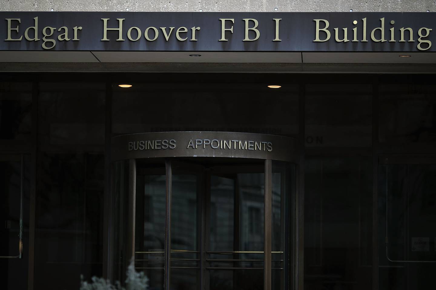 An entranceway to a building includes a revolving door. Above the door are letters that spell out business appointments. On the facade above, letters spell out Edgar Hoover FBI Building.