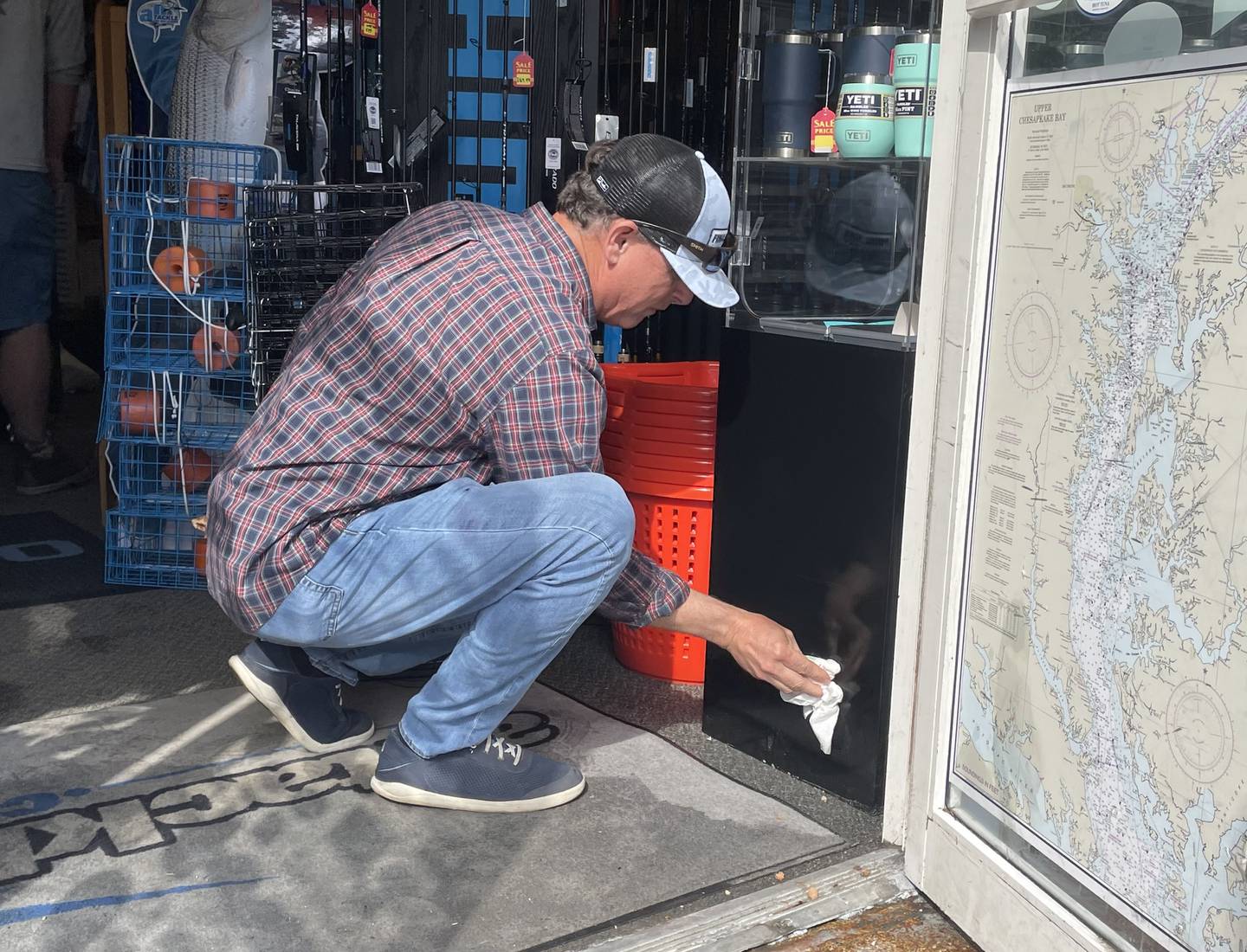 Keith Fraser, owner of alltackle.com, wipes blood stains from a case inside the doorway of his business on Friday, May 5, 2023. Just after 2 p.m. a man seeking help for gunshot wounds entered the threshold. He was taken to a hospital by ambulance where he later died.
