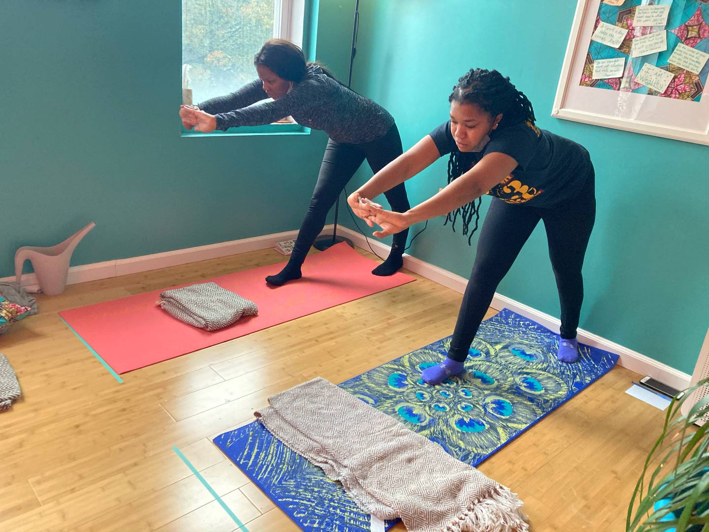 Two women stand in triangle pose and stretch their arms forward during a yoga class at Ama Yoga Wellness in West Baltimore.