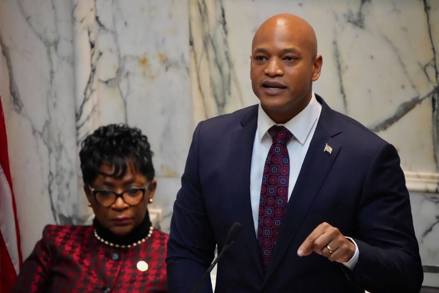 Gov. Wes Moore, in a blue suit, gestures as he gives his State of the State speech. Behind Moore, House Speaker Adrienne A. Moore wears a black and red outfit.