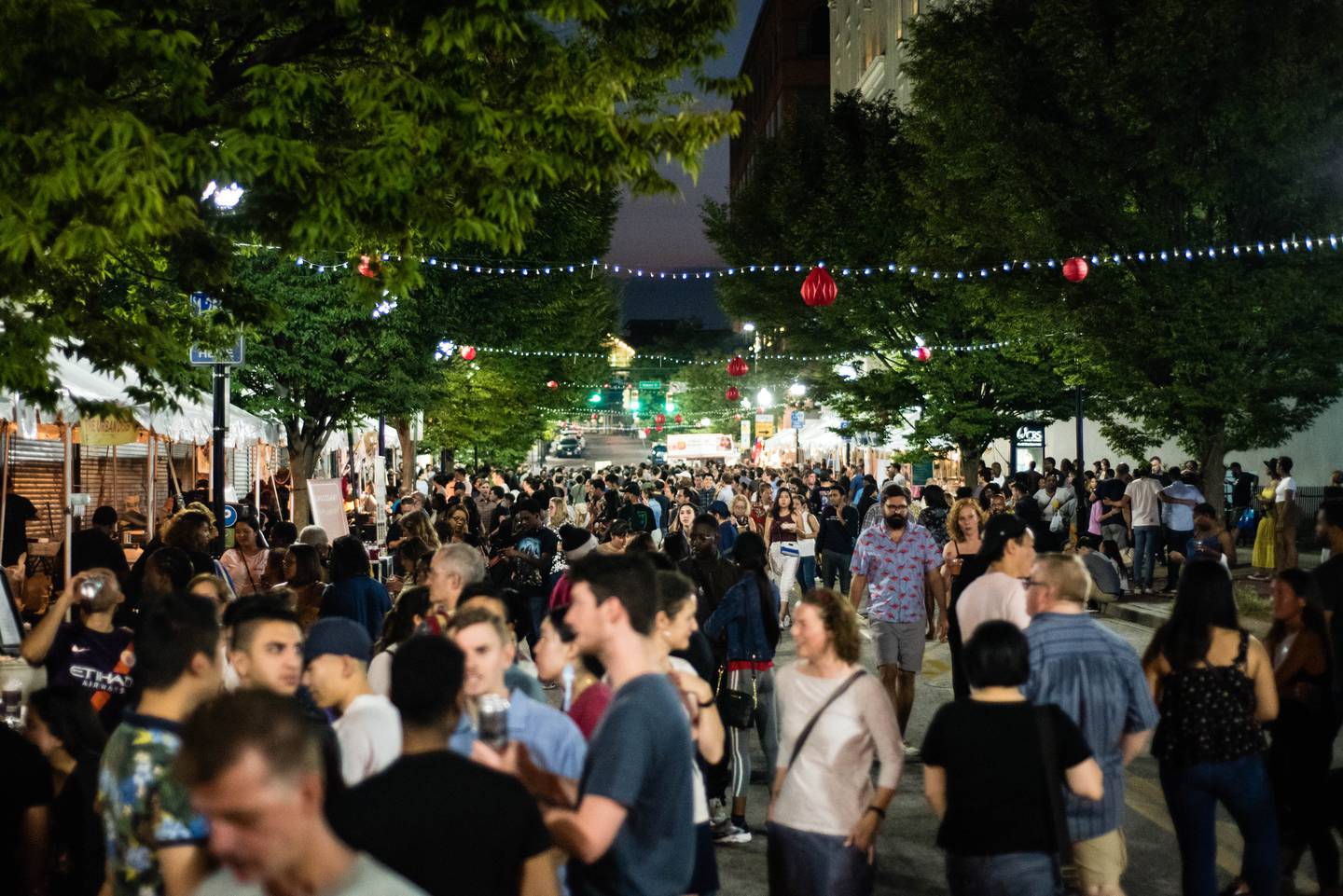 Festive red lanterns hang above a crowded street lined with tents full of food vendors at the 2019 Charm City Night Market.