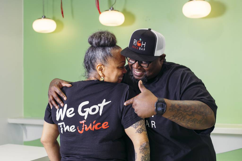 Dani and Michael Battle, owners of RICH Juice Bar, show off their company shirts inside their new location in the Light Street Pavilion, on Wednesday, April 17, 2024.