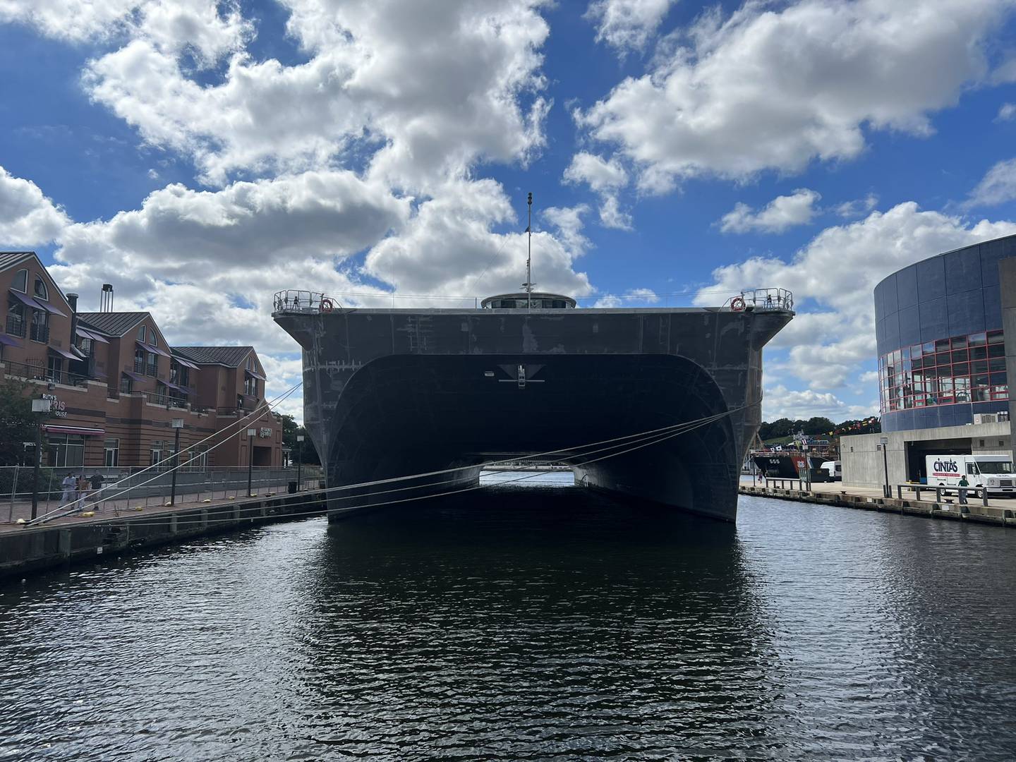 A large twin-hulled transport ship docked between two piers in Baltimore's harbor.