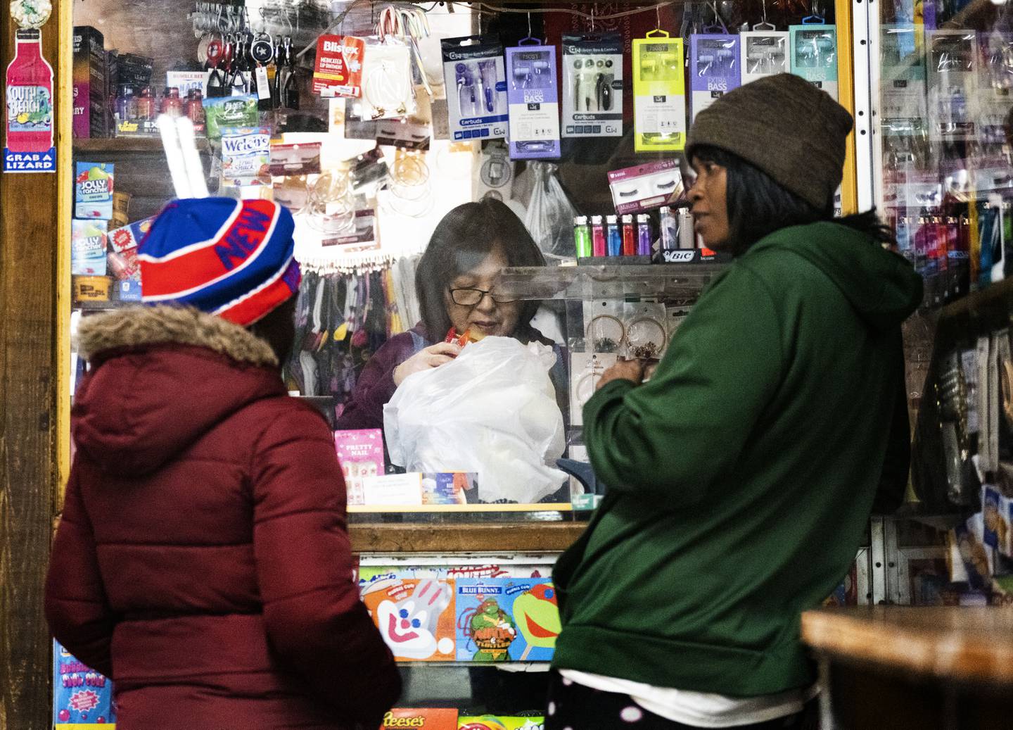 Tae Soon Lee bags the goods bought by Crystal William, 35, (left) and Nelvina Owens, 48, (right)at Lee's Mini Market, in Baltimore, Thursday, December 1, 2022.