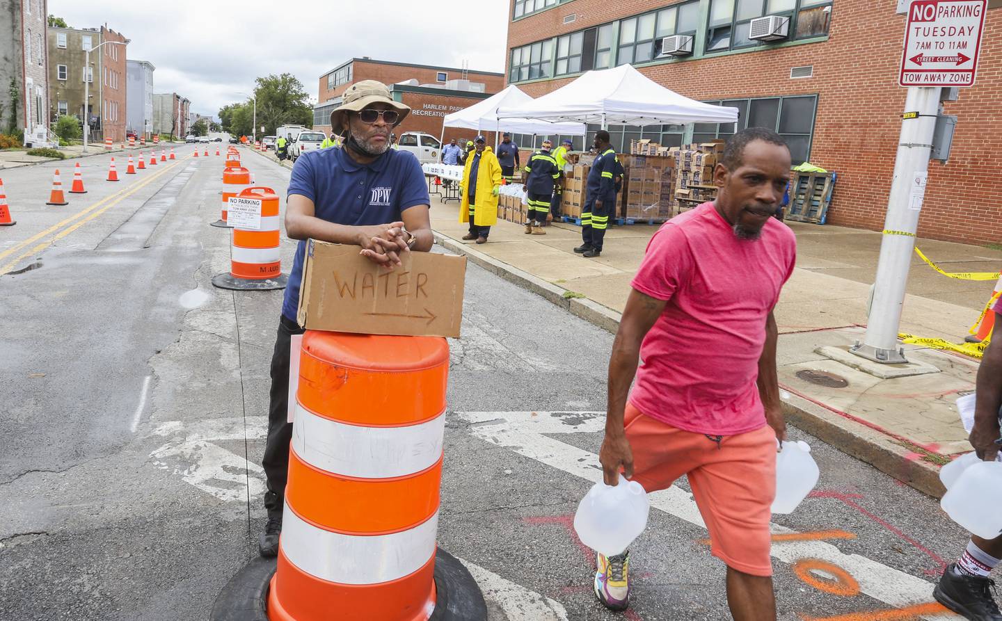 Charles Jackson of DPW guides residents to the water line where each resident received several gallons of water. Baltimore officials are advising residents of the Sandtown-Winchester and Harlem Park neighborhoods to boil their water before drinking it. E.coli was detected in samples taken from three addresses.