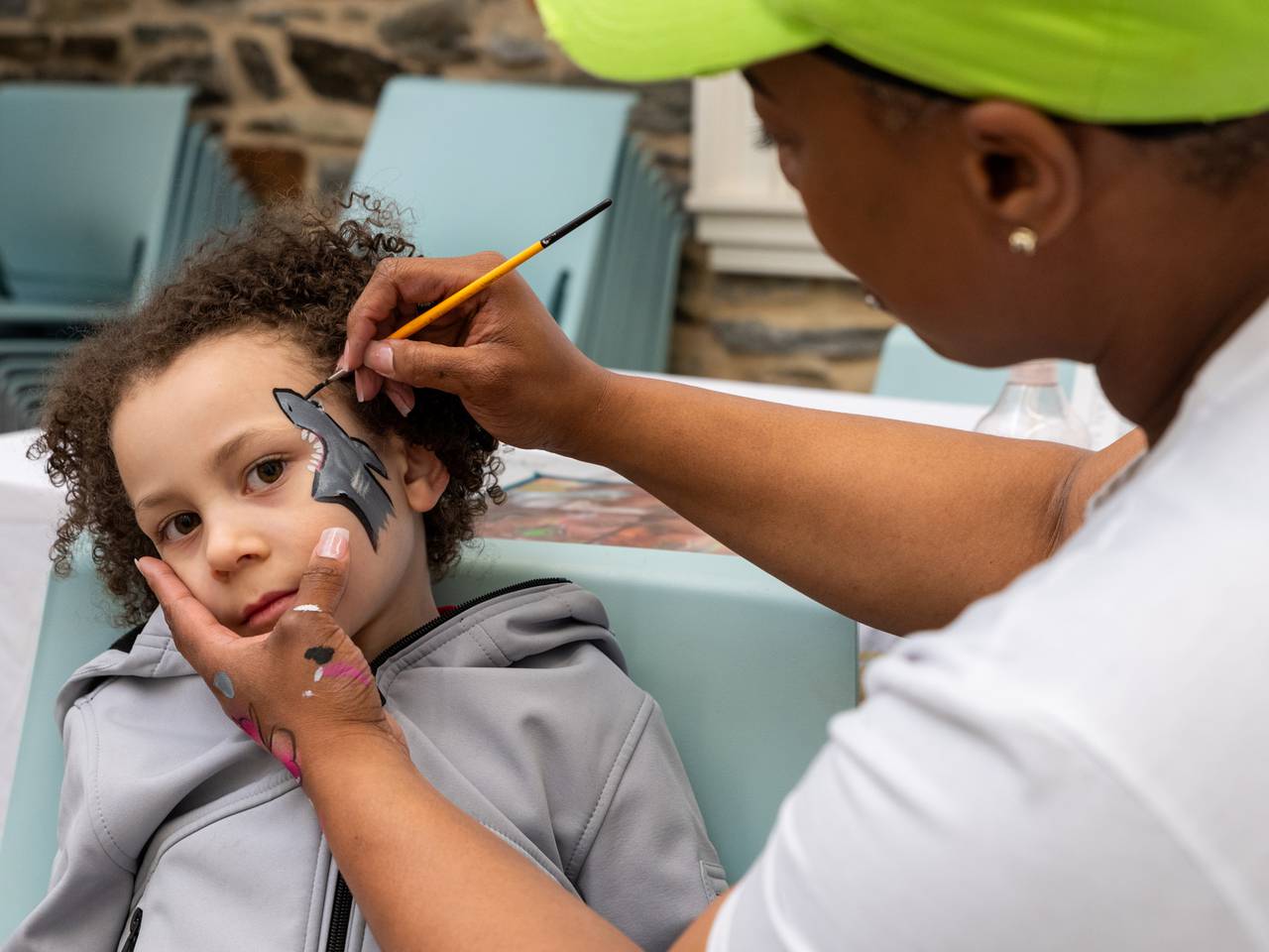 Adam Creek Rohner, 6, has a shark painted on his face by Sherae Davis of S. Cultured Creative Studios. Parks & People Easter Egg Hunt, Mar 30 2024, Baltimore, MD.