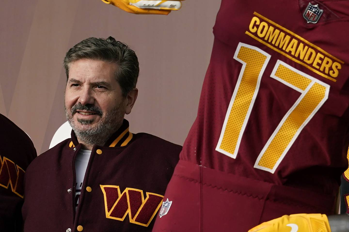 This photo shows Washington Commanders owner Dan Snyder standing near a jersey for the team.