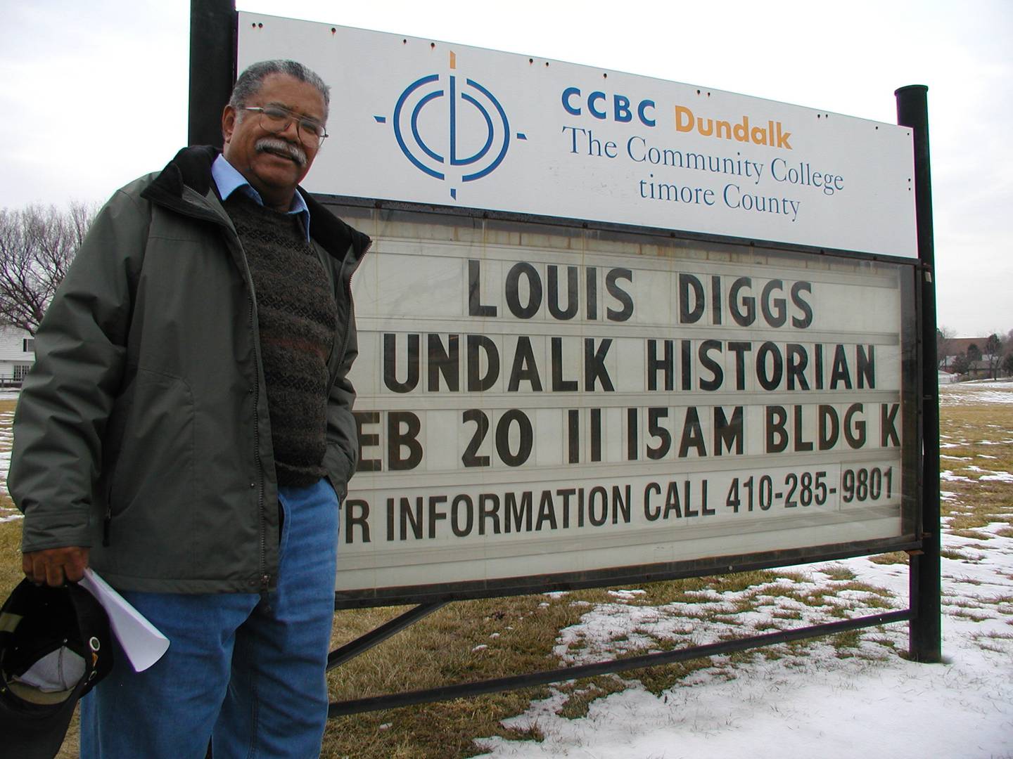 Community historian Louis Diggs stands in front of a sign promoting one of his talks. After Diggs died last year, many colleagues said he was irreplaceable.